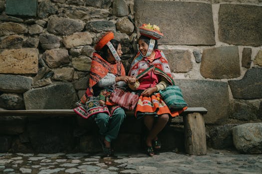 Two Peruvian women in traditional clothing share a moment on a bench in Ollantaytambo, Perú.