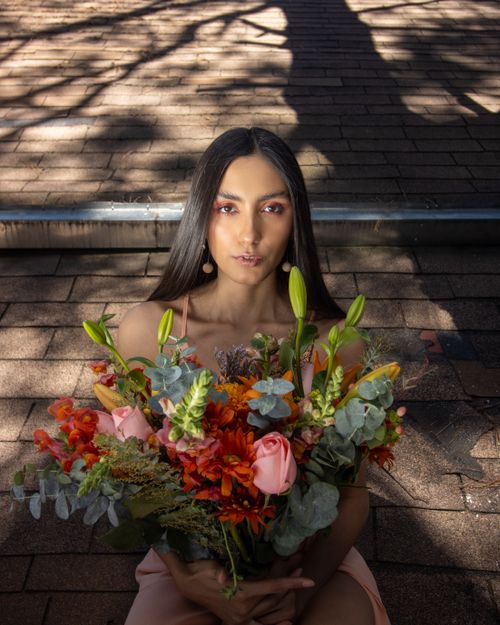 Free A woman poses gracefully with a large bouquet of vibrant flowers on a rooftop setting. Stock Photo