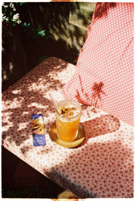 Chilled beverage with ice and garnishes on a sunny patterned bench outdoors.