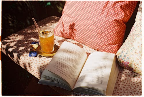 Free Summer Drink and a Book on a Patterned Bench with Pillows Stock Photo