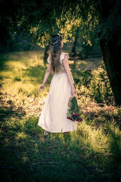 young woman in cottage core dress and corset standing holding a bouquet in a park