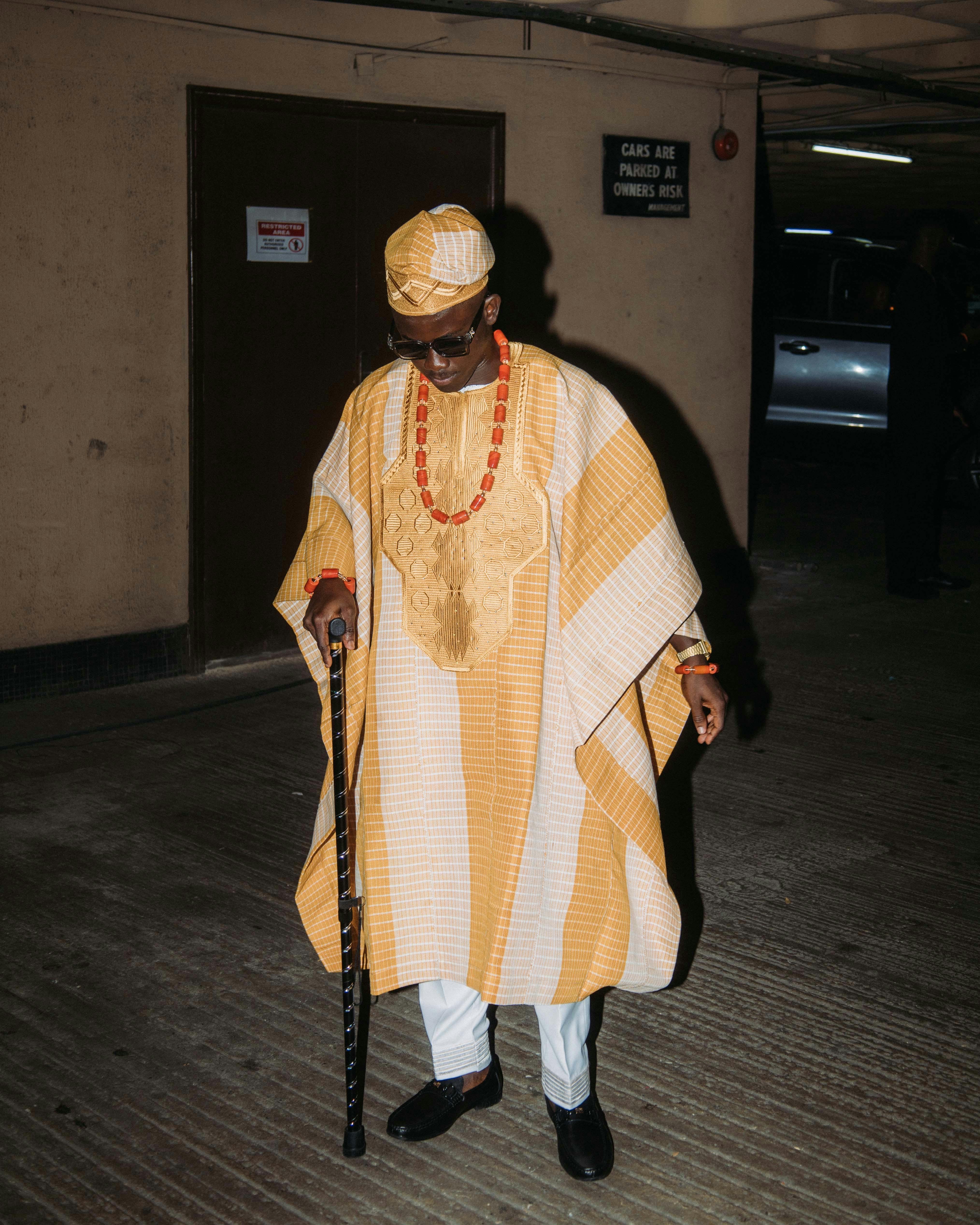 Elegant African man wearing traditional Yoruba attire with a walking stick and accessories.