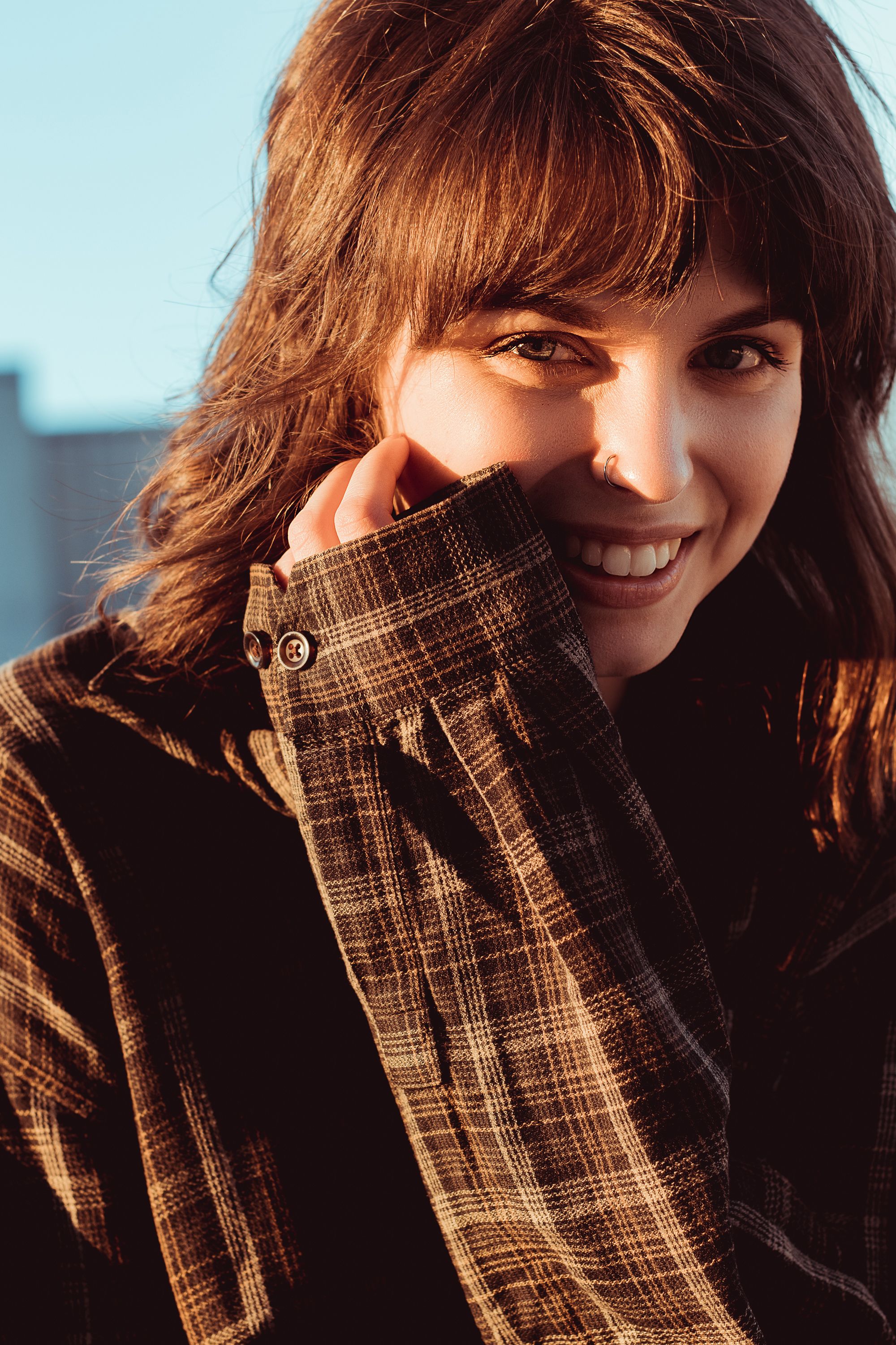 Portrait of a young woman with brown hair smiling in sunlight.
