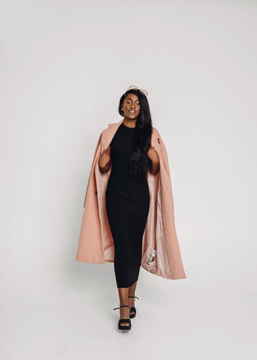 Free Chic woman in a black dress and pink coat showcases modern elegance on a white background. Stock Photo