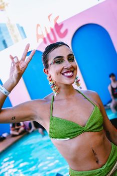 Smiling woman in green bikini posing by the poolside making a V sign.