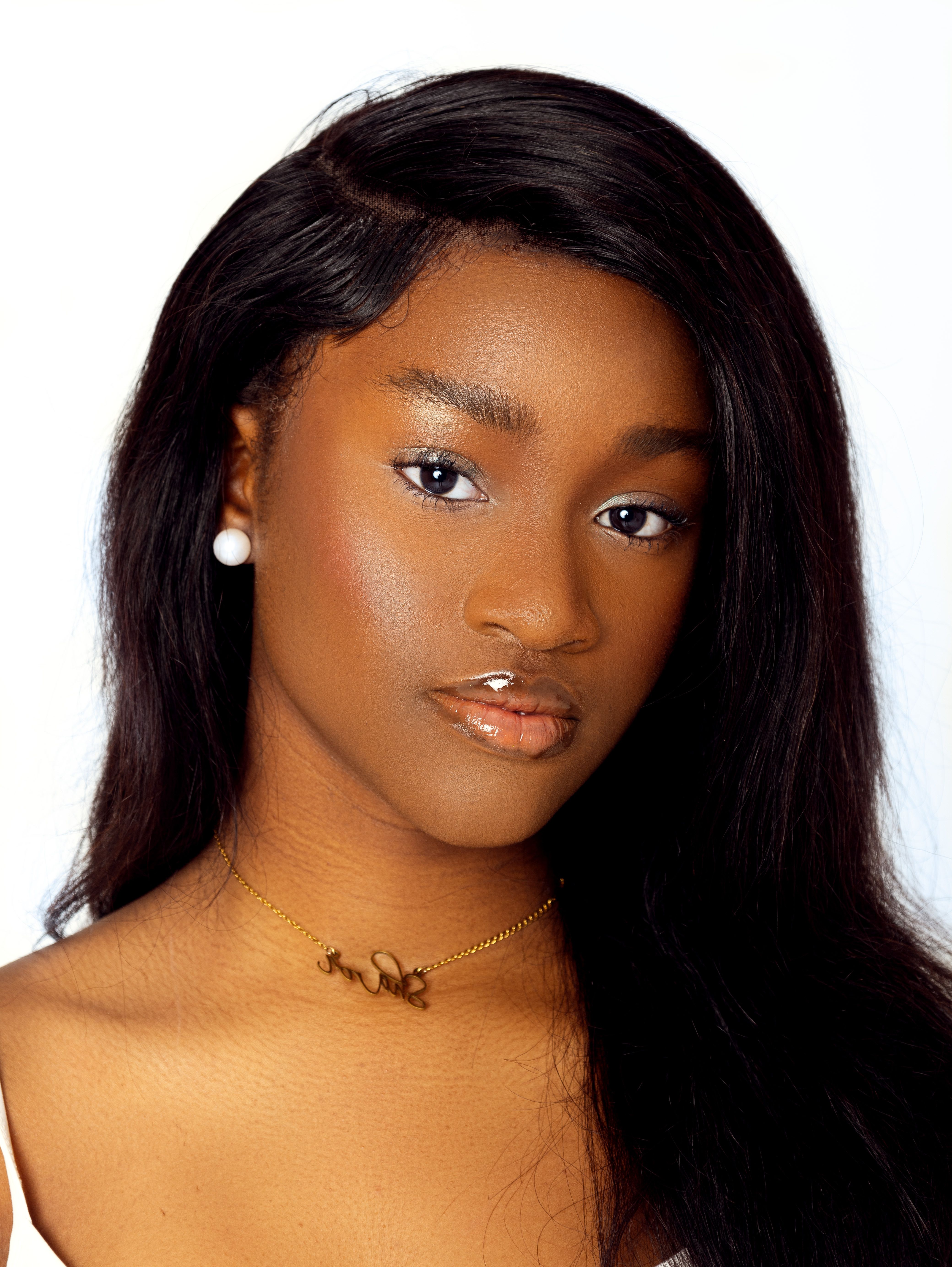Studio portrait of a woman with long hair, wearing earrings and a necklace against a plain background.