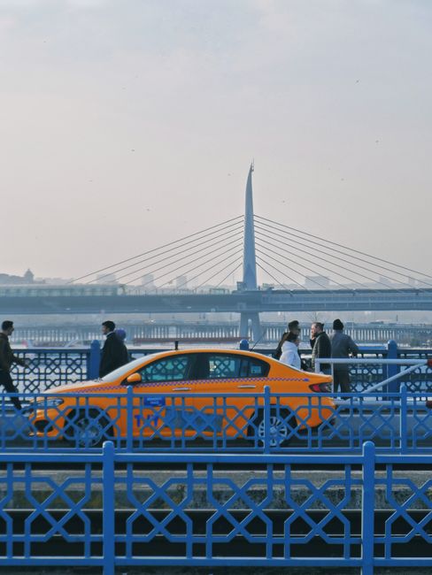Busy scene on Galata Bridge, Istanbul, featuring pedestrians and an orange taxi.