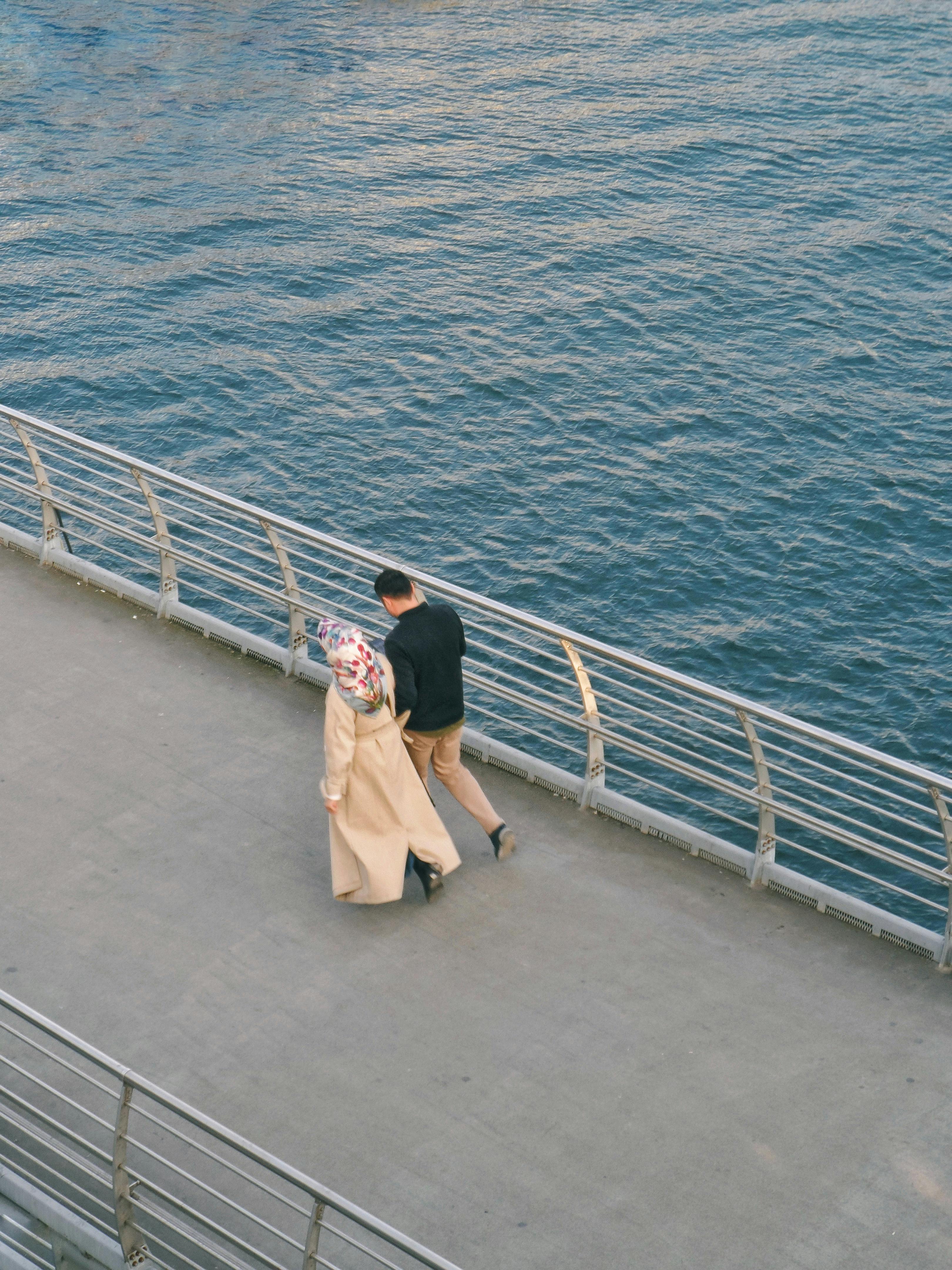 A couple strolls on a footbridge by the sea in Istanbul, Türkiye, capturing romance and tranquility.