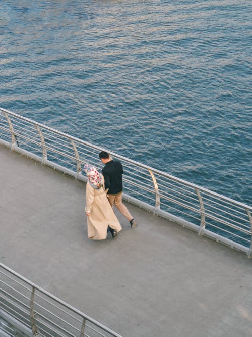 A couple walking along the water near a bridge