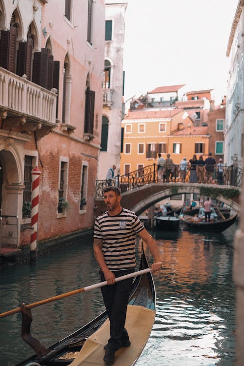 A man in striped shirt rides a gondola down a canal