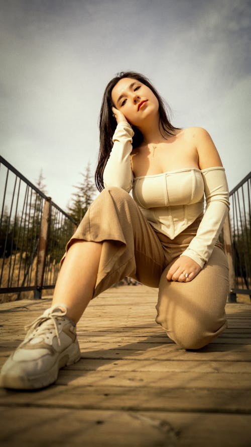 A woman in a white top and pants sitting on a wooden bridge