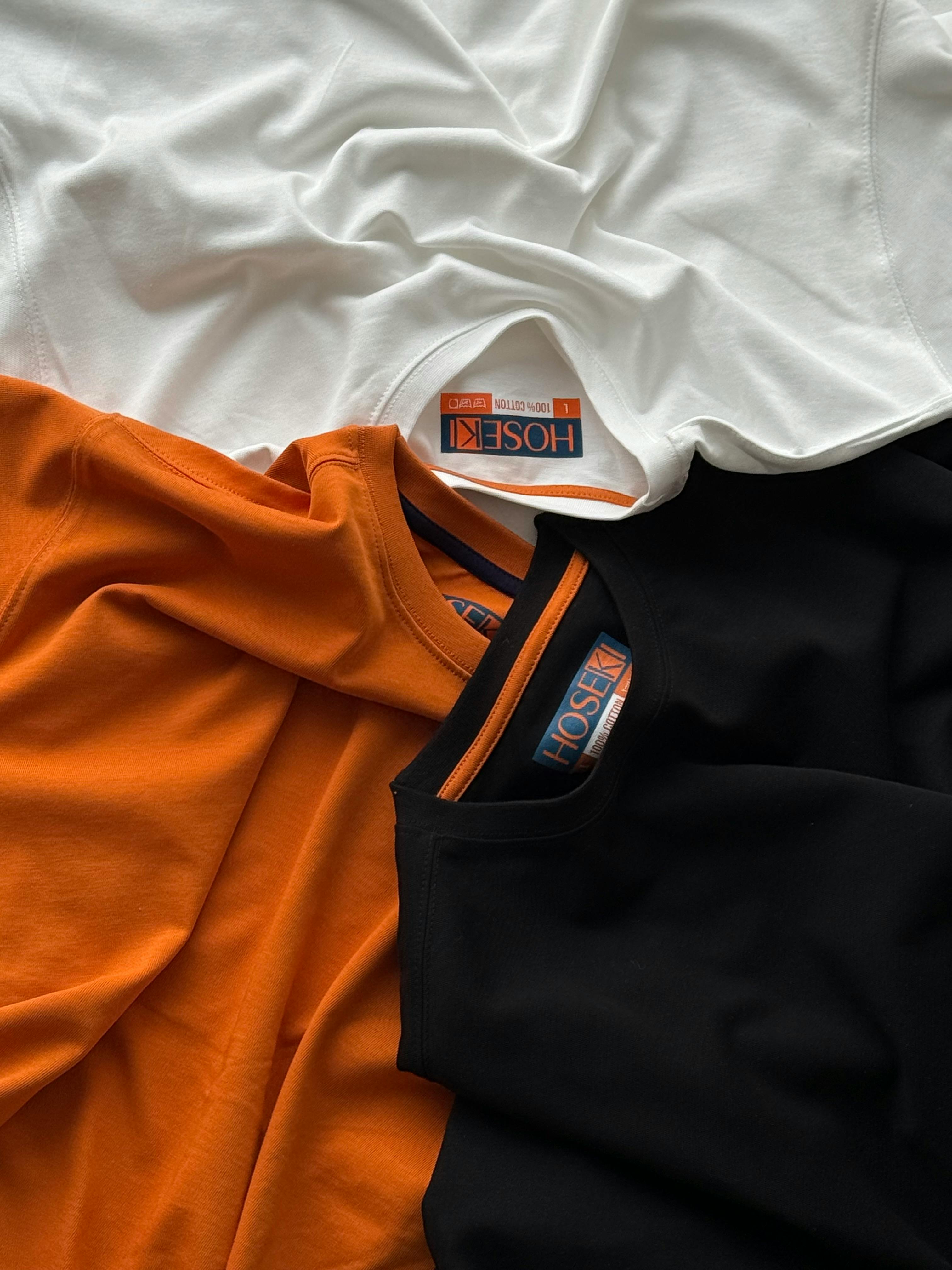 A collection of vibrant cotton T-shirts in white, orange, and black showcased in a flat lay.