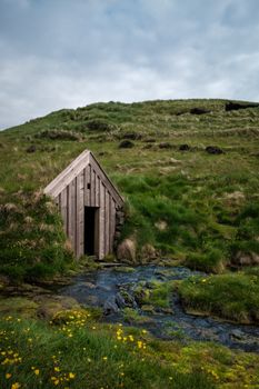 A traditional Icelandic turf house surrounded by lush greenery and a gentle stream.