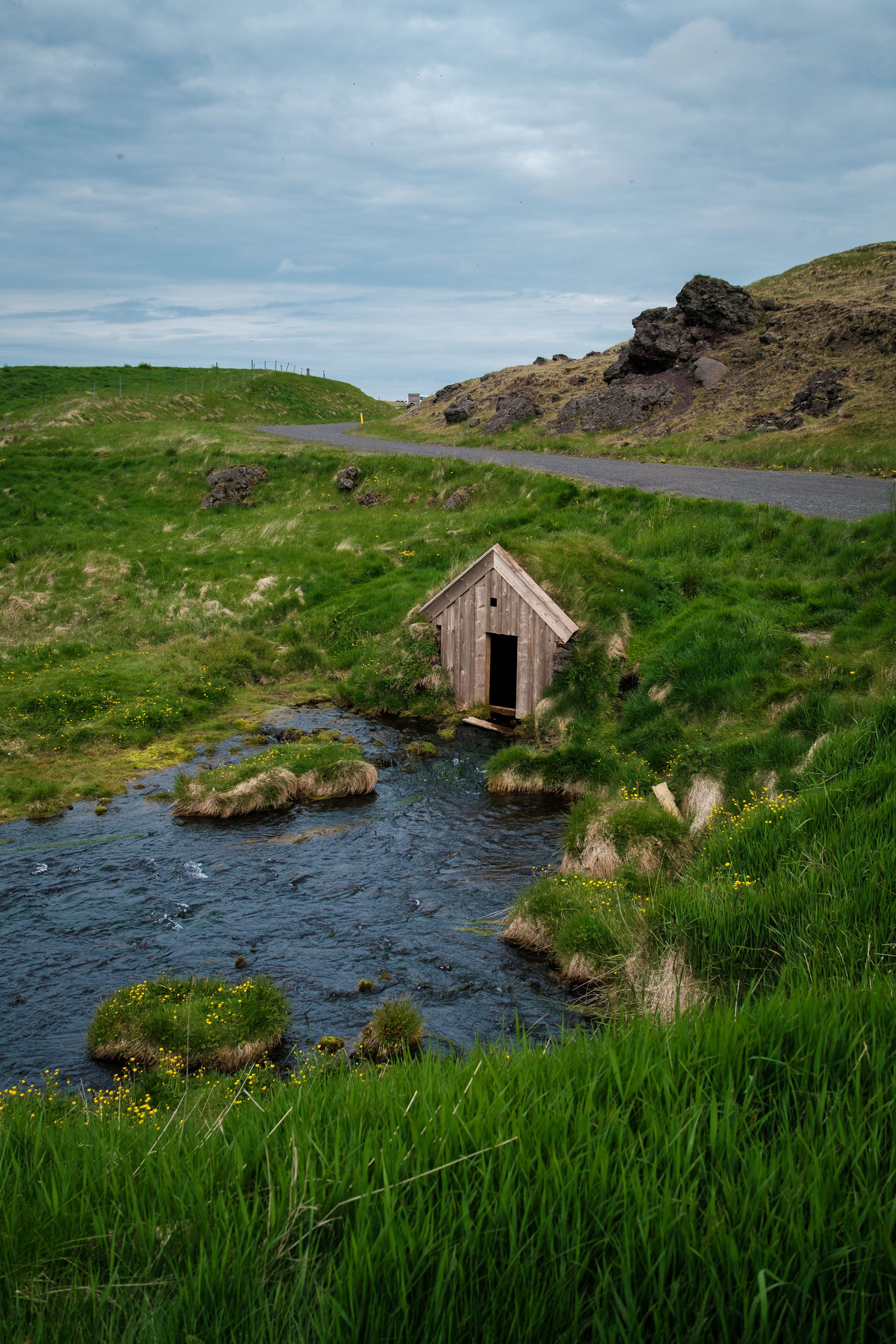 A charming Keldur Turf House nestled in the green Icelandic landscape by a serene stream.