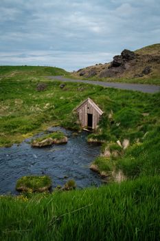 A charming Keldur Turf House nestled in the green Icelandic landscape by a serene stream.