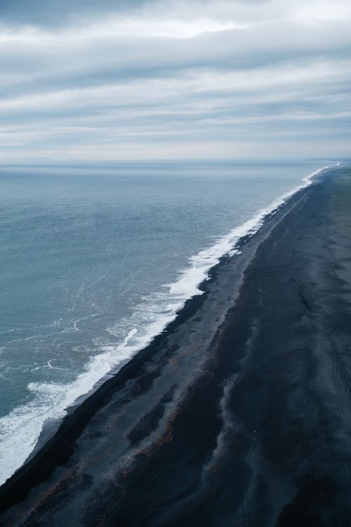 Free Stunning drone shot of Iceland's black sand beach with ocean waves against the shore. Stock Photo