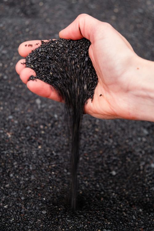 Free Close-up of a hand pouring black pebbles onto the ground, showcasing texture and depth. Stock Photo
