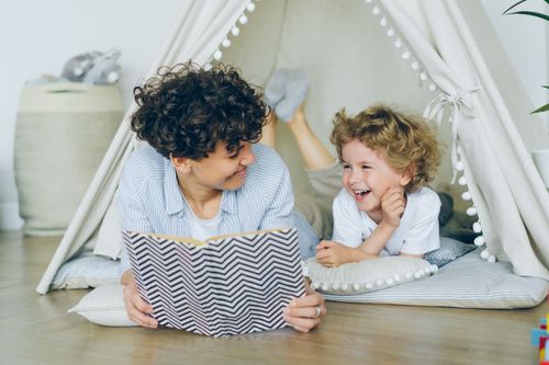 Free A joyful mother and son enjoying reading together in a cozy indoor tent setting. Stock Photo