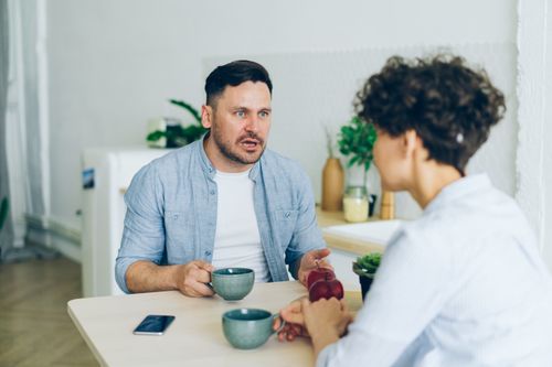 Free Couple having a serious conversation at the kitchen table with coffee cups. Stock Photo