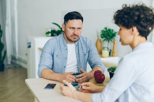 Angry Man Sitting by Table and Looking at Woman