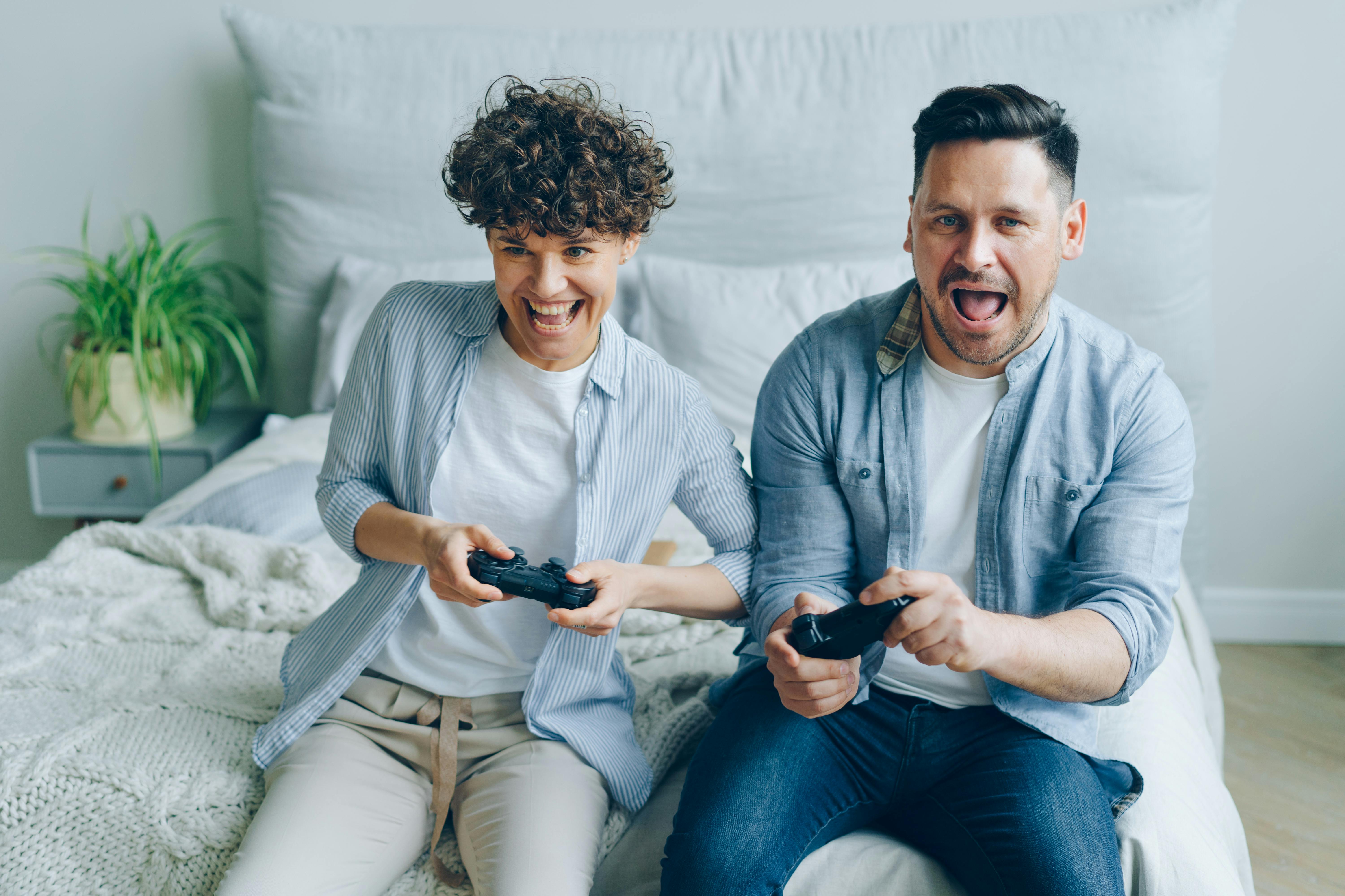 a couple sitting on a bed and playing a video game