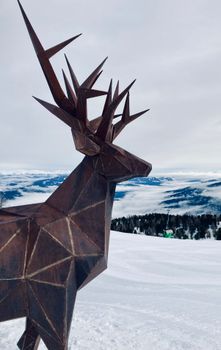 Polygonal deer sculpture overlooking a snowy mountain landscape, creating a striking winter scene.