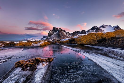 Snowy mountains and shallow stream meadow at pink purple dusk