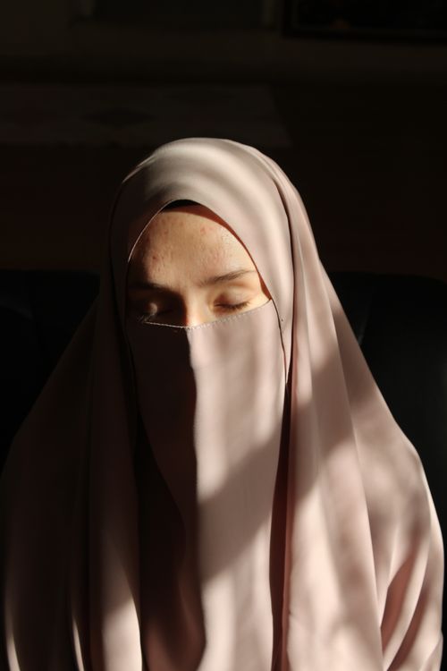 Free A serene portrait of a woman wearing a pink niqab, softly lit by the sun. Stock Photo