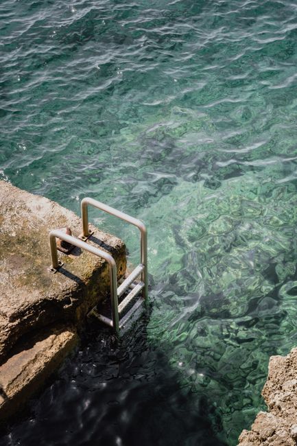 Metal ladder along a rocky shore in Cannes, France, leading into turquoise waters.