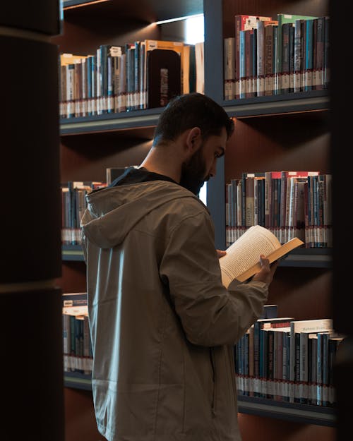 A man in a jacket is reading a book in a library