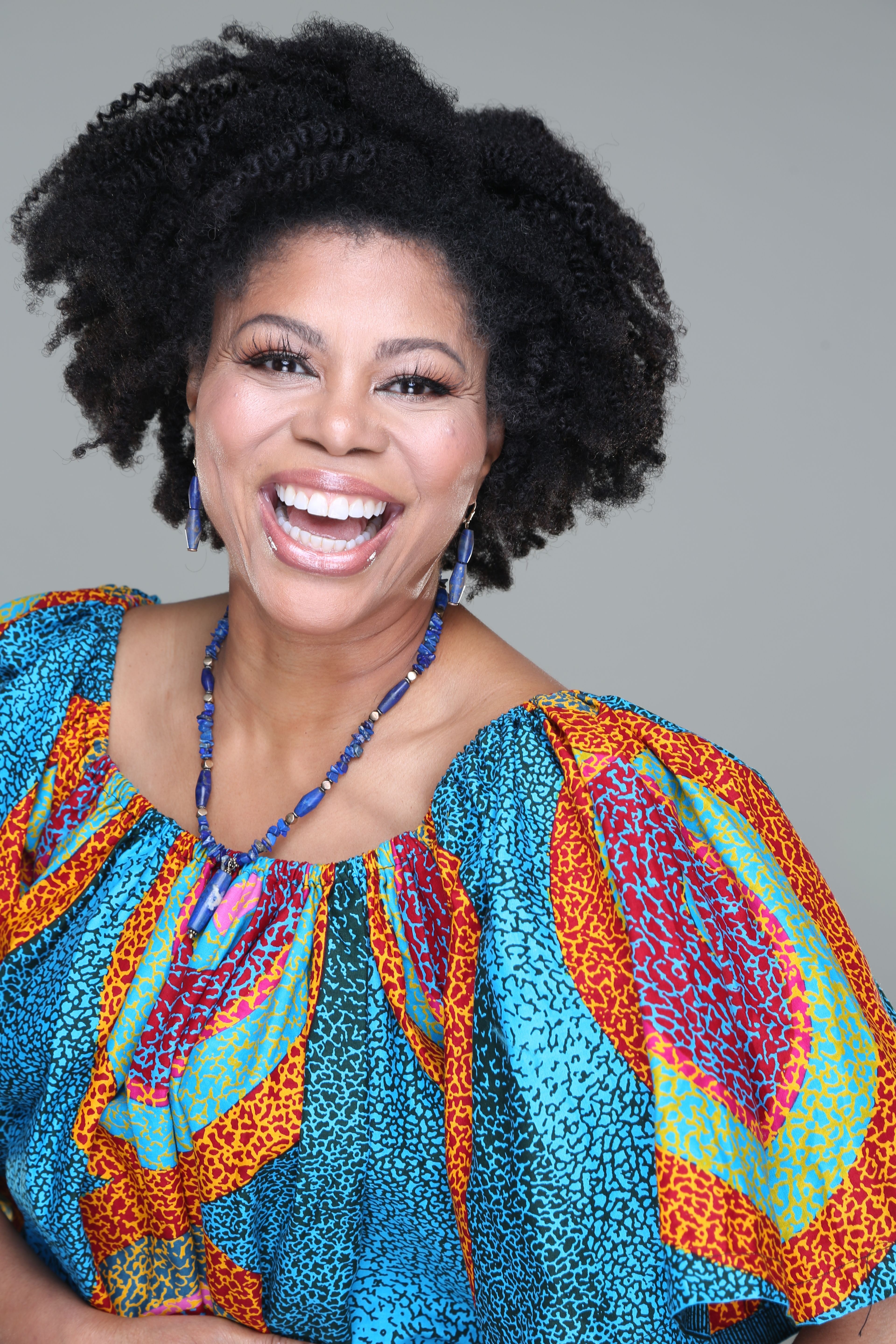 Colorful studio portrait of an adult woman laughing joyfully, wearing vibrant clothing.