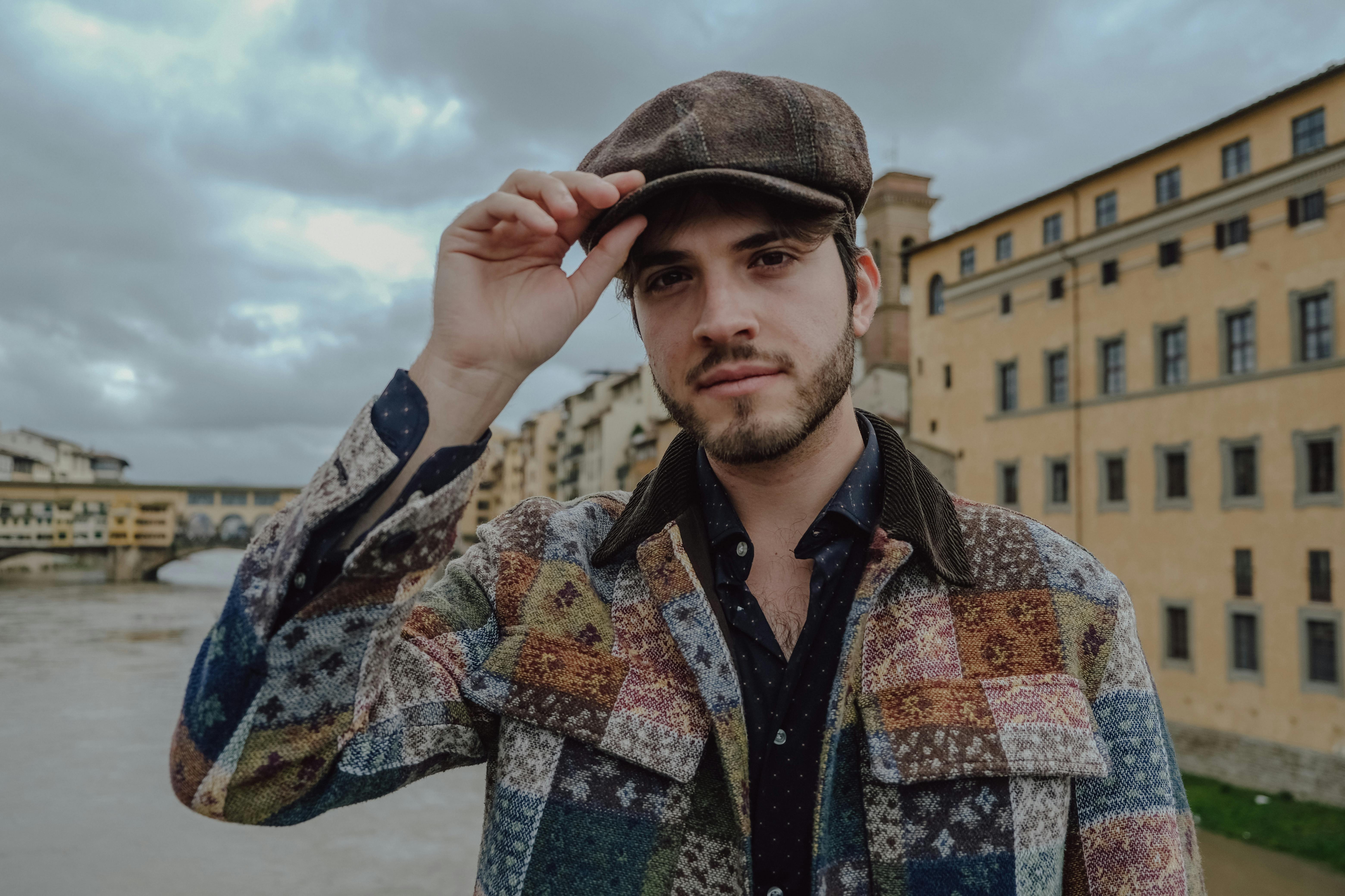 Stylish traveler near an Italian bridge wearing a patchwork jacket, reflecting personal style with a classic backdrop.