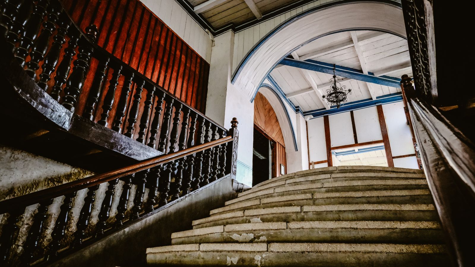 Escalier ancien à rampe en bois ouvragé et arcades, dans le hall d'un immeuble de rapport.