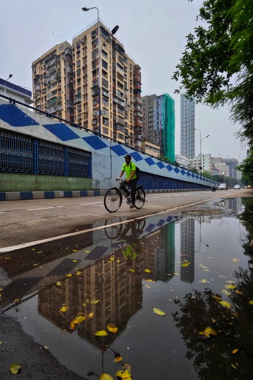 Free A cyclist rides beside a reflective puddle on a Kolkata city street. Stock Photo