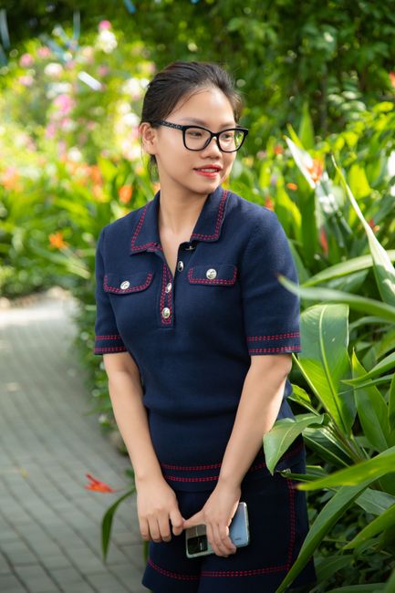 Asian woman in glasses and fashionable outfit surrounded by vibrant plants outdoors in Hanoi park.