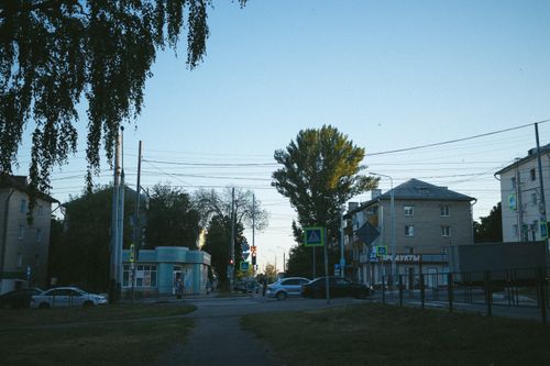 Free An urban intersection with buildings and trees during twilight, featuring visible signs and street elements. Stock Photo