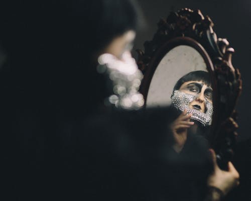 A woman with a face mask is looking in a mirror