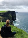 在爱尔兰克莱尔郡，一个女人坐在莫赫悬崖上欣赏着令人惊叹的景色
