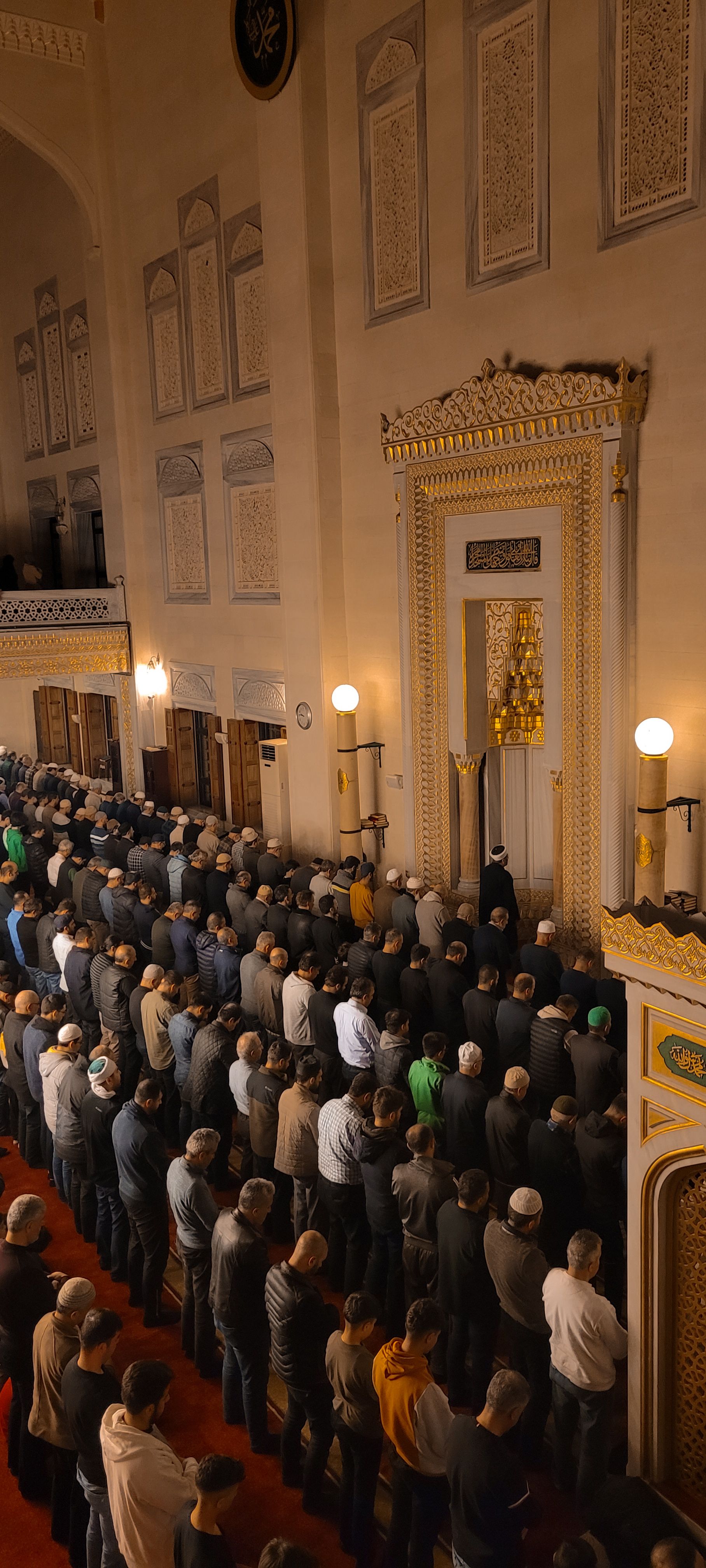 Men are gathered in an ornate mosque interior for prayer, emphasizing Islamic religious traditions.