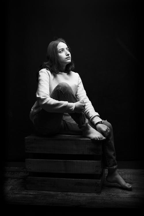 Free Grayscale Photo of Woman Sitting on a Wooden Crate While Looking Up Stock Photo