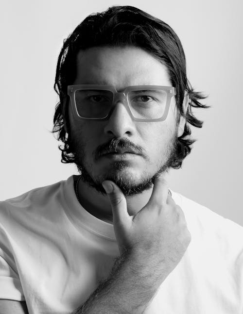 A man with glasses and a beard is posing for a black and white photo