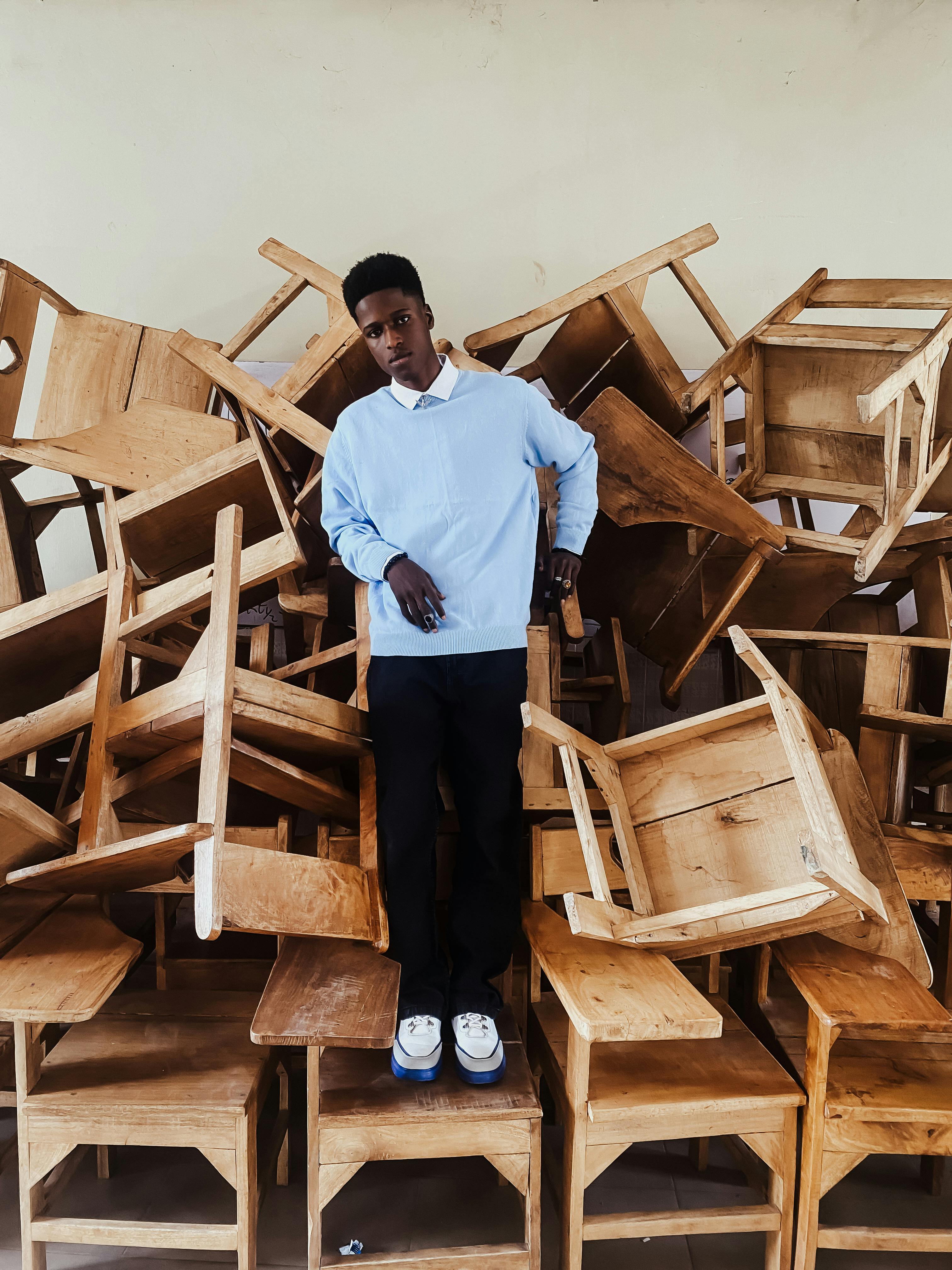 A fashionable individual posing among piled wooden chairs, showcasing urban style in Lagos, Nigeria.