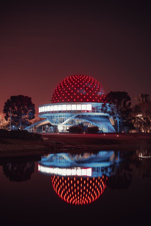 Free Stunning night view of the illuminated Galileo Galilei Planetarium in Buenos Aires, reflecting on water. Stock Photo