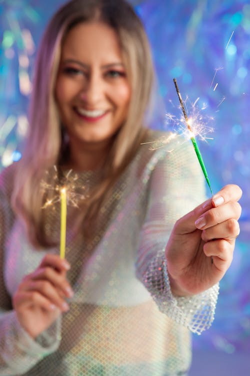 A woman holding sparklers in front of a colorful background