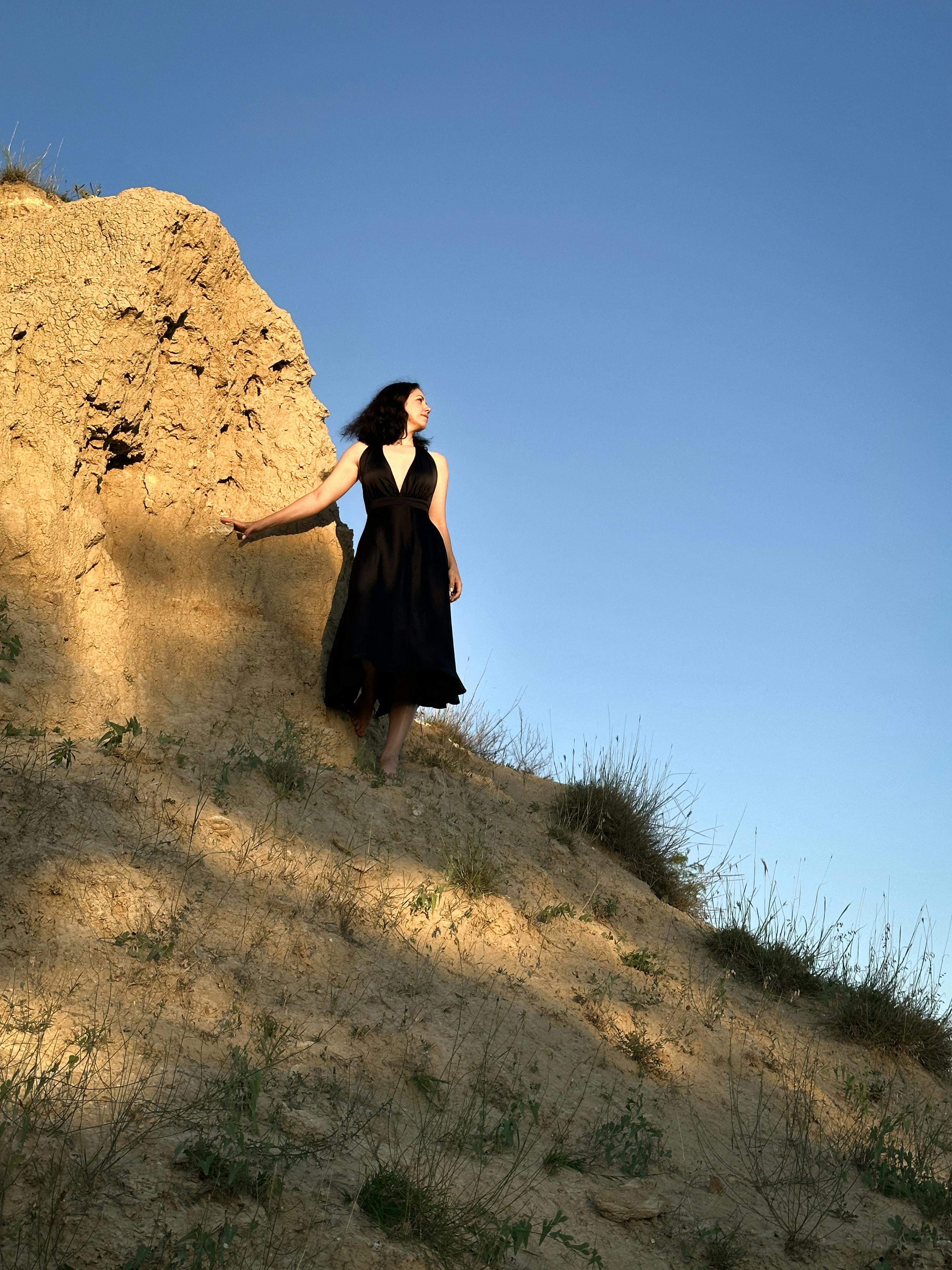 Woman in a black dress standing against a sunlit sandy hill under a clear blue sky in Ukraine.