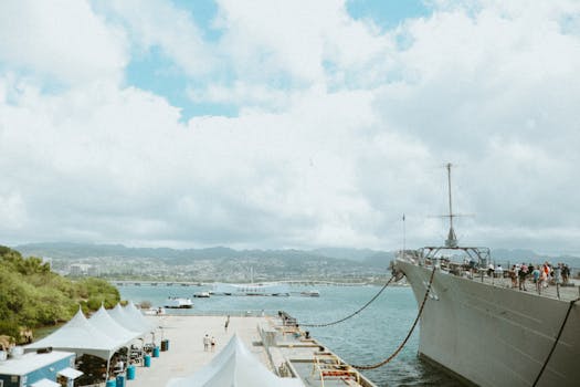 Large ship docked at a harbor with a mountain backdrop and cloudy sky in Hawaii.
