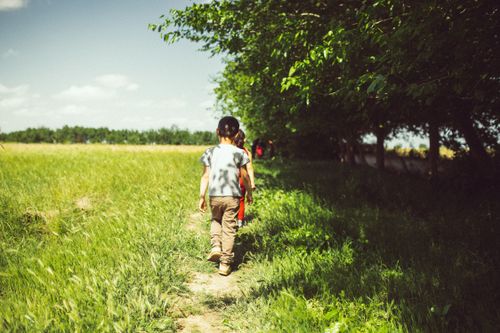 Free Two kids walking along a path under sunny skies in a green meadow. Stock Photo