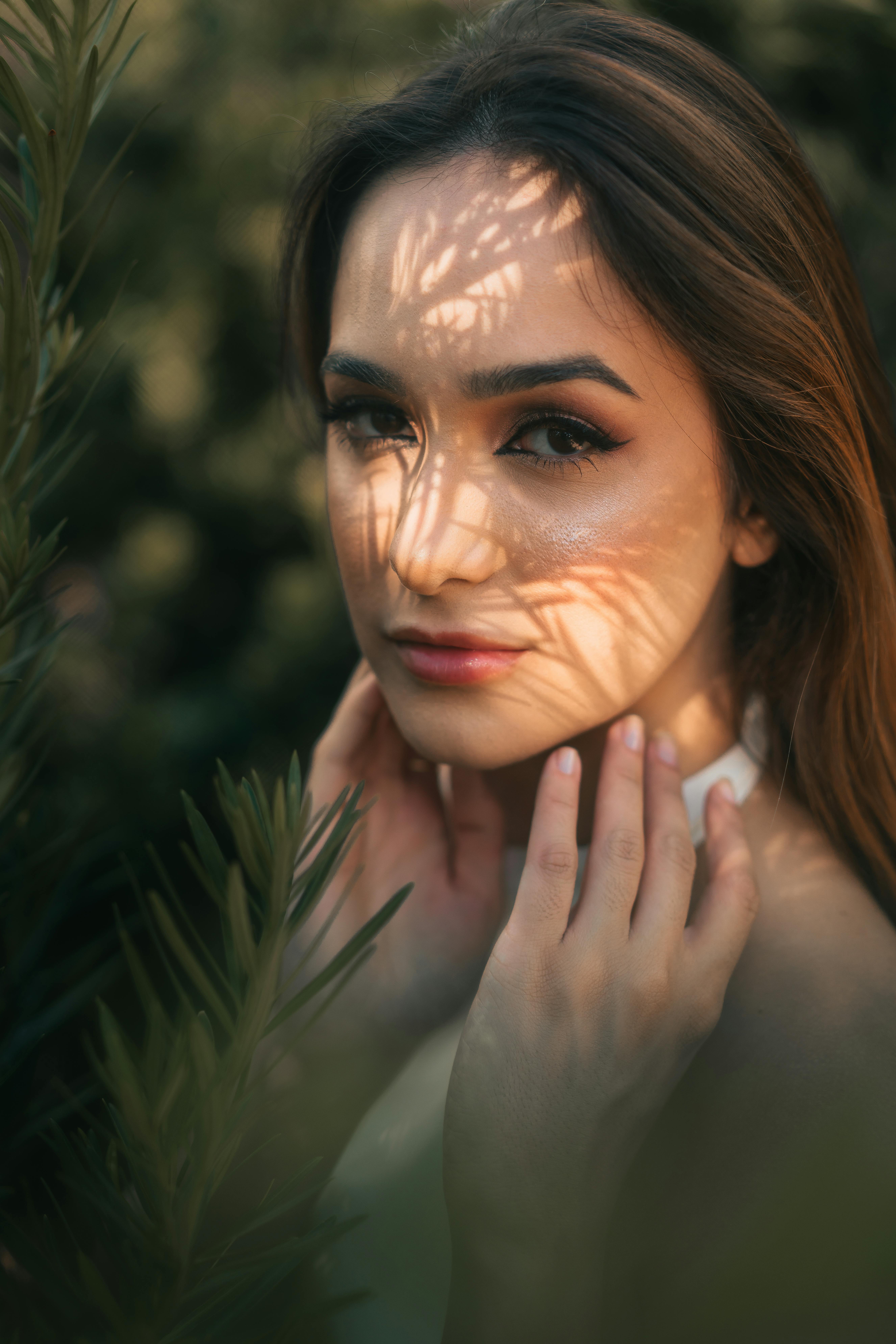Elegant portrait of a young woman amidst natural foliage, creating artistic light patterns on her fa