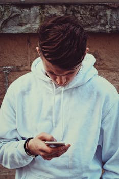 一名穿着白色连帽衫的成年男子在户外对着砖墙使用智能手机