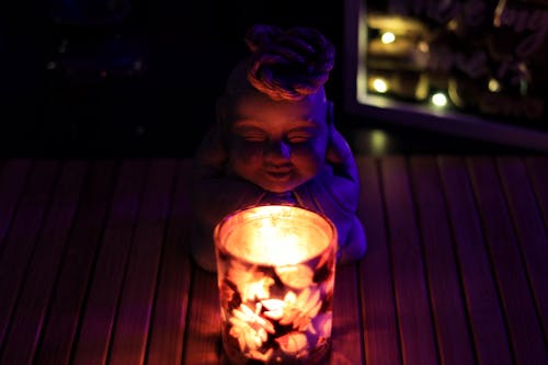 Free Close-up of a Burning Candle and a Figurine Standing on a Table  Stock Photo